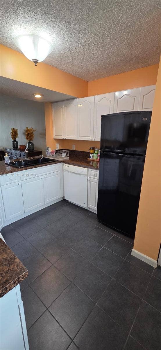 115 Lake Emerald Drive, #408, Oakland Park, FL 33309 Kitchen featuring white cabinetry, dark stone-finish countertops, black-finish sink, large-format tile flooring, and integrated appliances