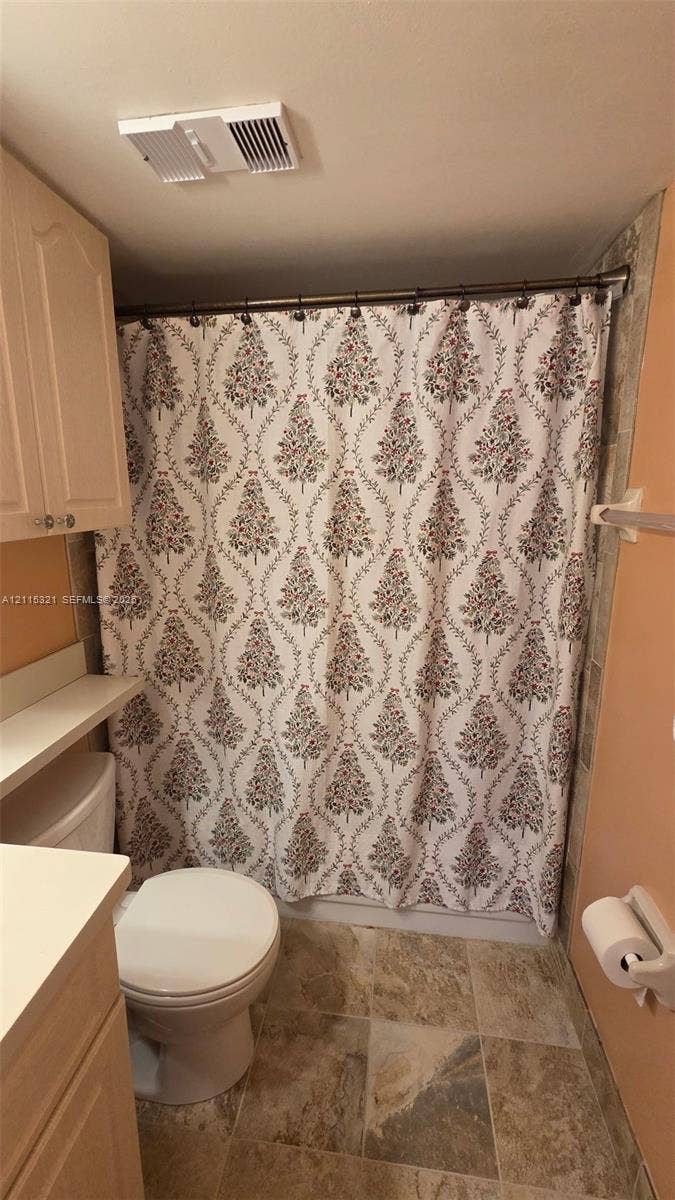 115 Lake Emerald Drive, #408, Oakland Park, FL 33309 Bathroom featuring light-finish cabinetry, neutral solid-surface countertop, stone-finish tile flooring, and a wall-mounted towel bar