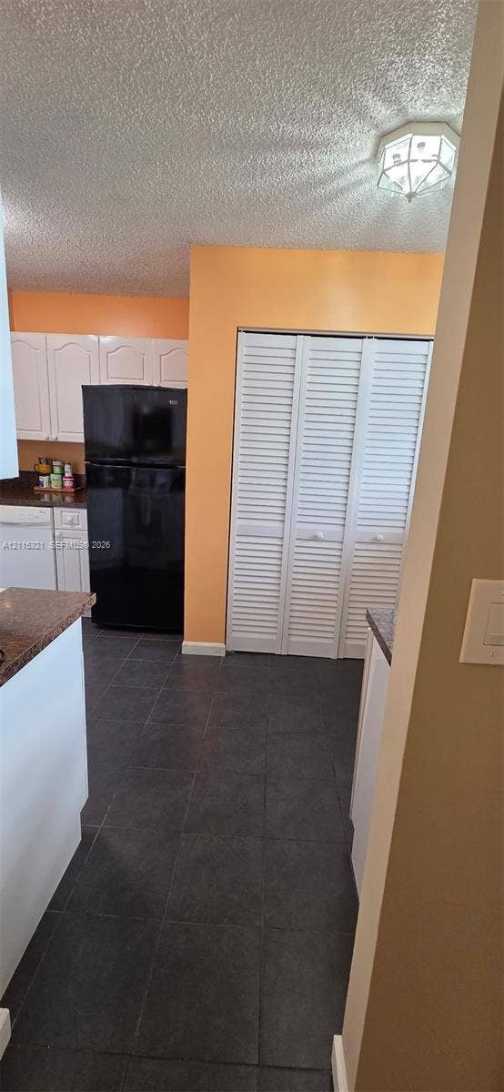 115 Lake Emerald Drive, #408, Oakland Park, FL 33309 Kitchen featuring dark stone-finish countertops, white cabinetry, dark tile flooring, and white louvered bifold closet doors