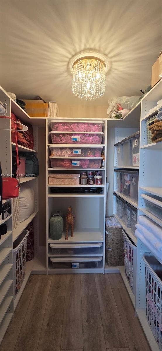 115 Lake Emerald Drive, #408, Oakland Park, FL 33309 Custom walk-in closet featuring white built-in cabinetry, tiered shelving, integrated pull-out drawers, wood-finish flooring, and a decorative crystal flush-mount light fixture