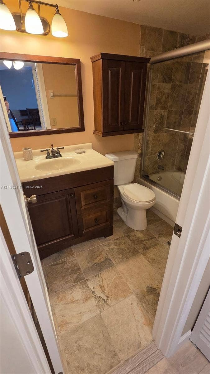 115 Lake Emerald Drive, #408, Oakland Park, FL 33309 Bathroom featuring a dark wood vanity with a stone countertop, a built-in wall cabinet, tiled flooring, and a shower-tub combination with tile surround