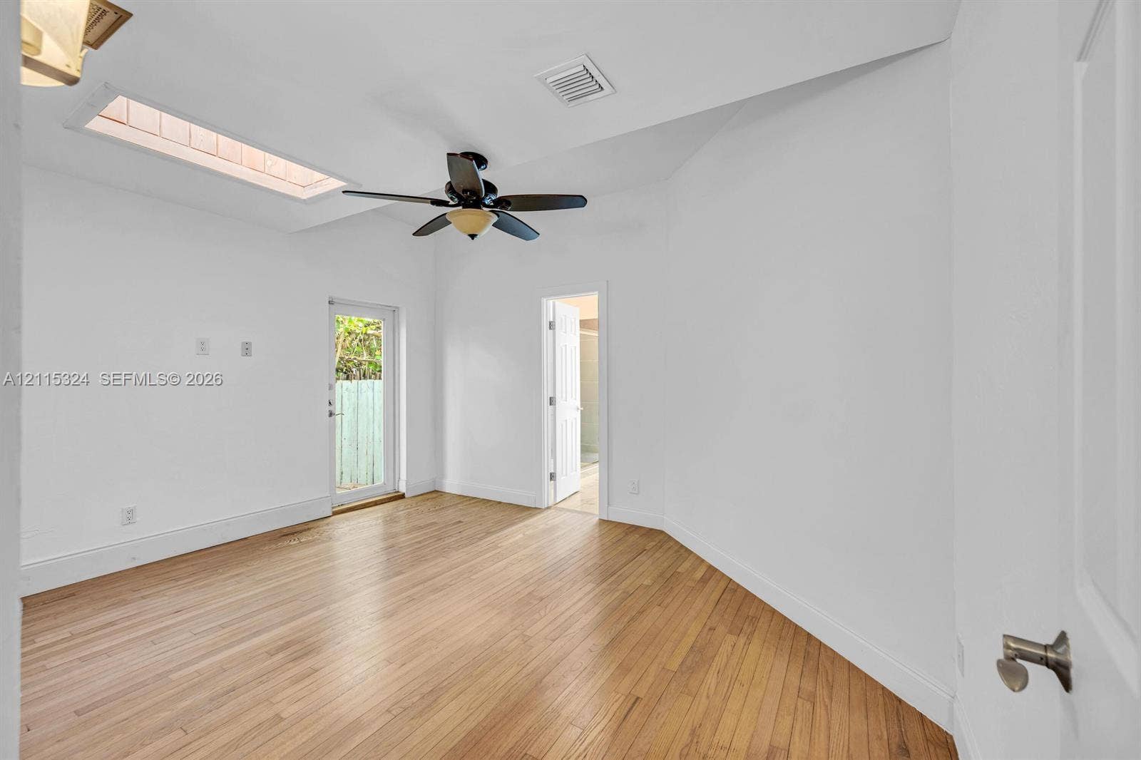 Interior space featuring wood-finish flooring, a vaulted ceiling with a skylight, a ceiling fan with integrated lighting, and an exterior glass-panel door