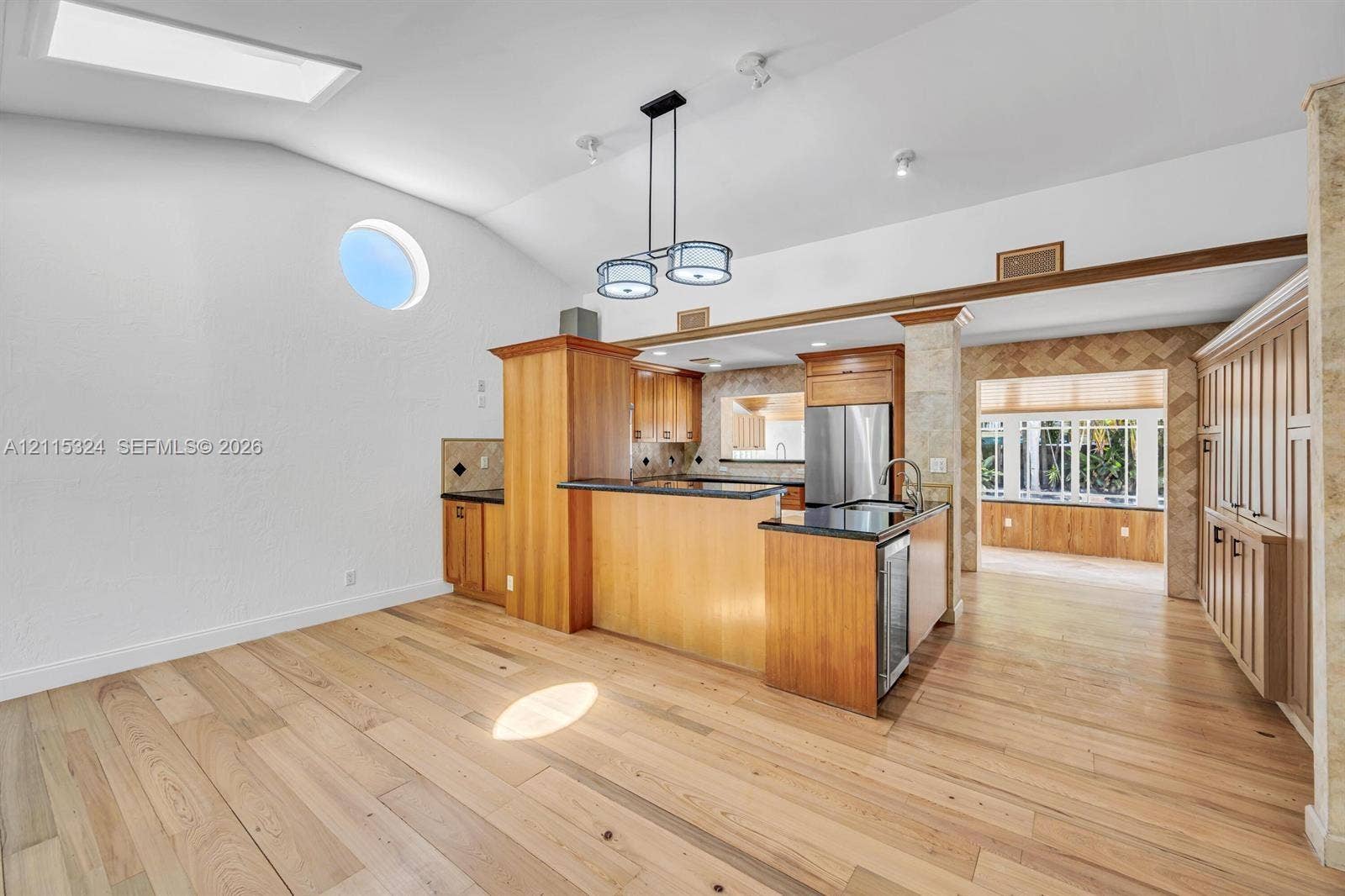 Vaulted ceilings featuring a skylight and circular accent window, wood-finish flooring, custom cabinetry with dark countertops, and a modern multi-pendant light fixture