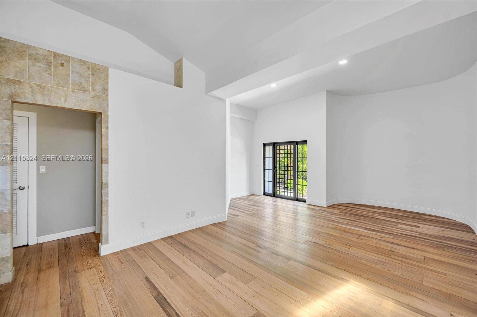 Interior featuring vaulted ceilings, wood-finish flooring, a curved wall, stone-accented doorway, and a multi-pane glass door