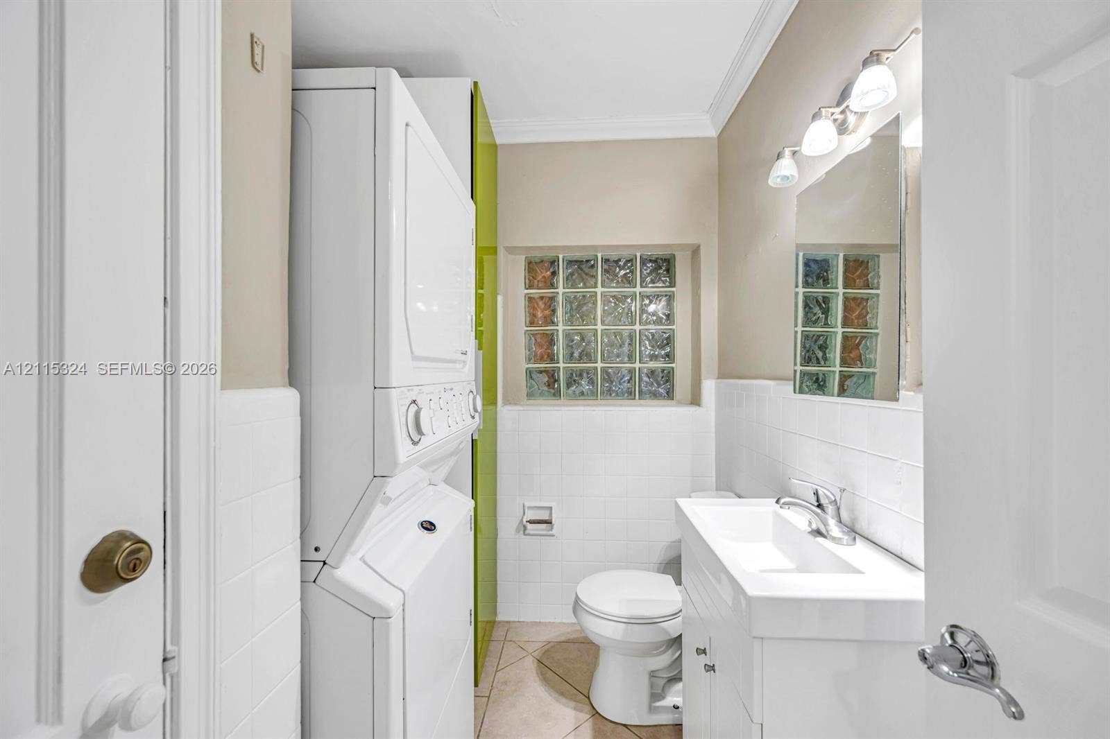 Combination laundry area and bathroom featuring a stacked washer and dryer, square glass block window, white vanity with integrated sink, and polished chrome fixtures