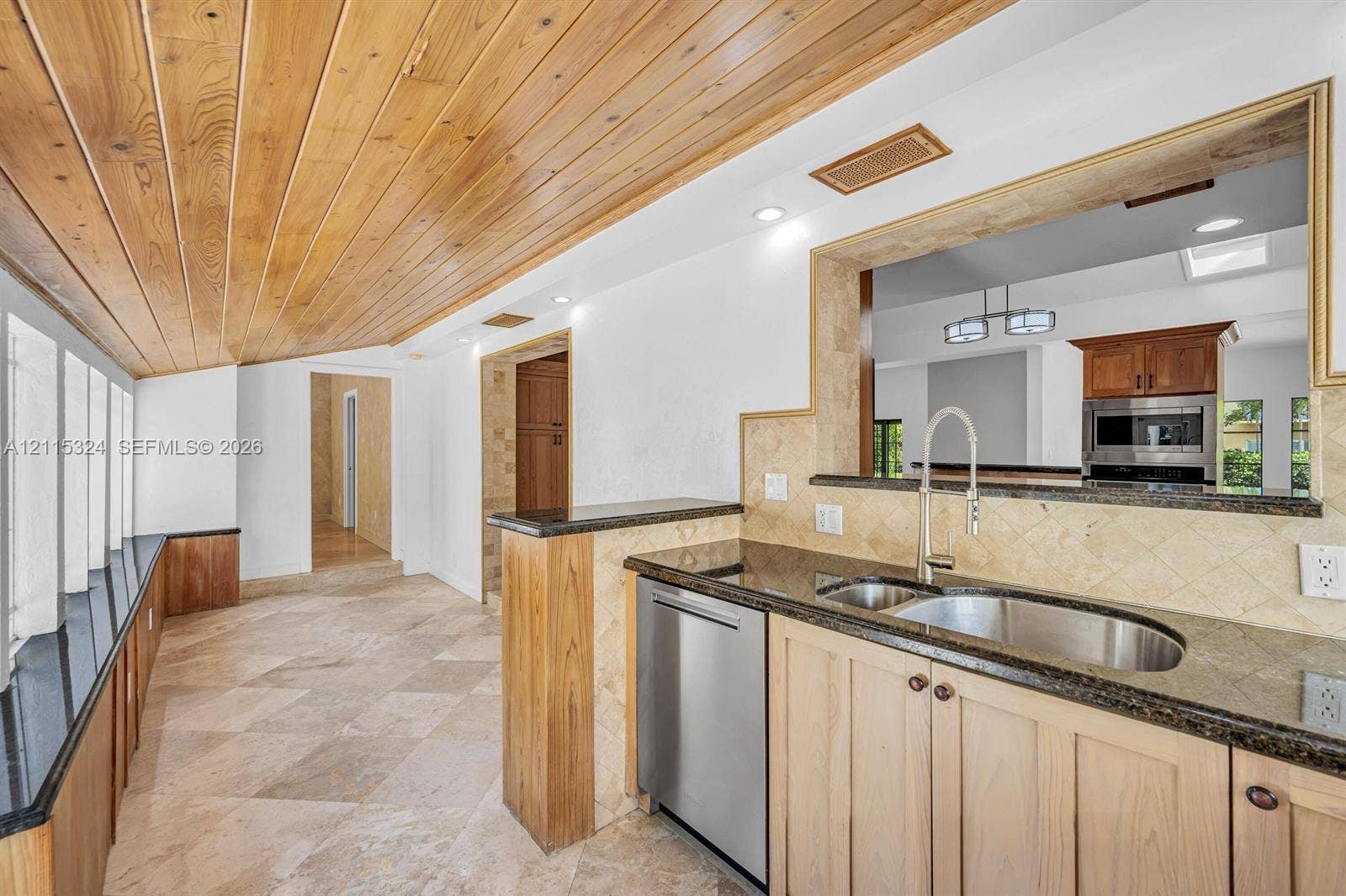 Vaulted natural wood plank ceiling, tile flooring, stone-finish countertops, stainless steel dual-basin sink, and built-in cabinetry