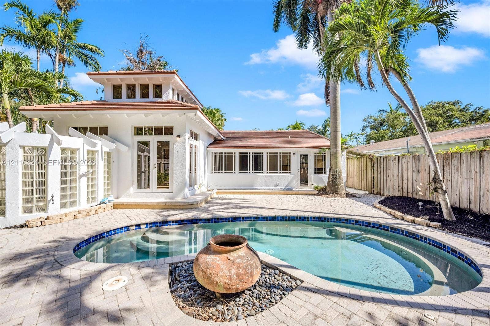 Custom-designed outdoor area featuring a swimming pool, integrated fountain, paver stone hardscaping, tiered architectural roofline, and glass block privacy wall