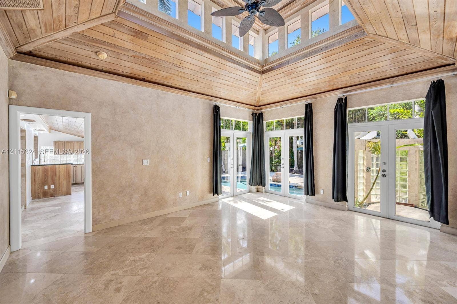 High-ceiling room featuring a wood-plank tray ceiling, central skylight, polished stone flooring, and three sets of glass-paned double doors
