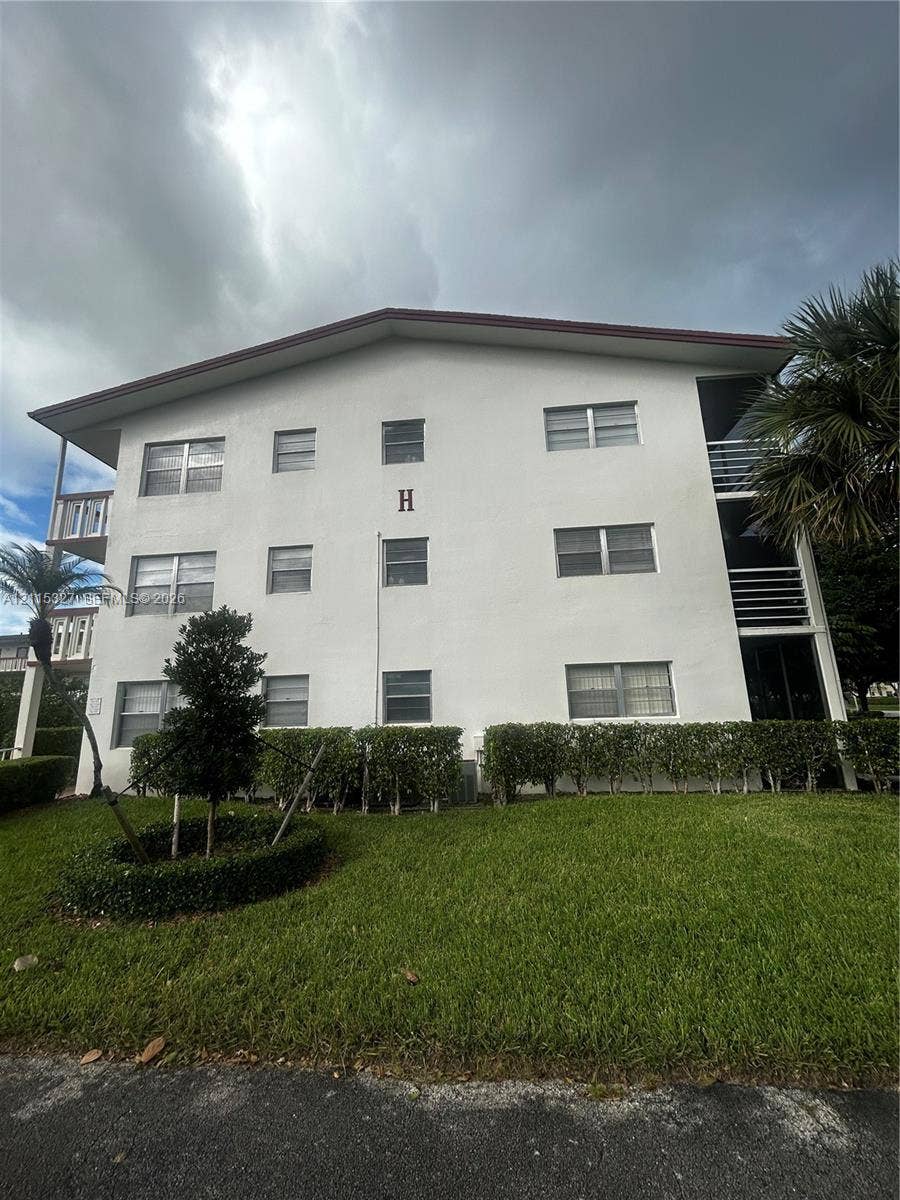 335 Brighton H, #H, Boca Raton, Boca Raton, FL 33434 Three-story exterior featuring a light-toned facade, horizontal sliding windows, covered balconies with railings, and manicured shrubbery