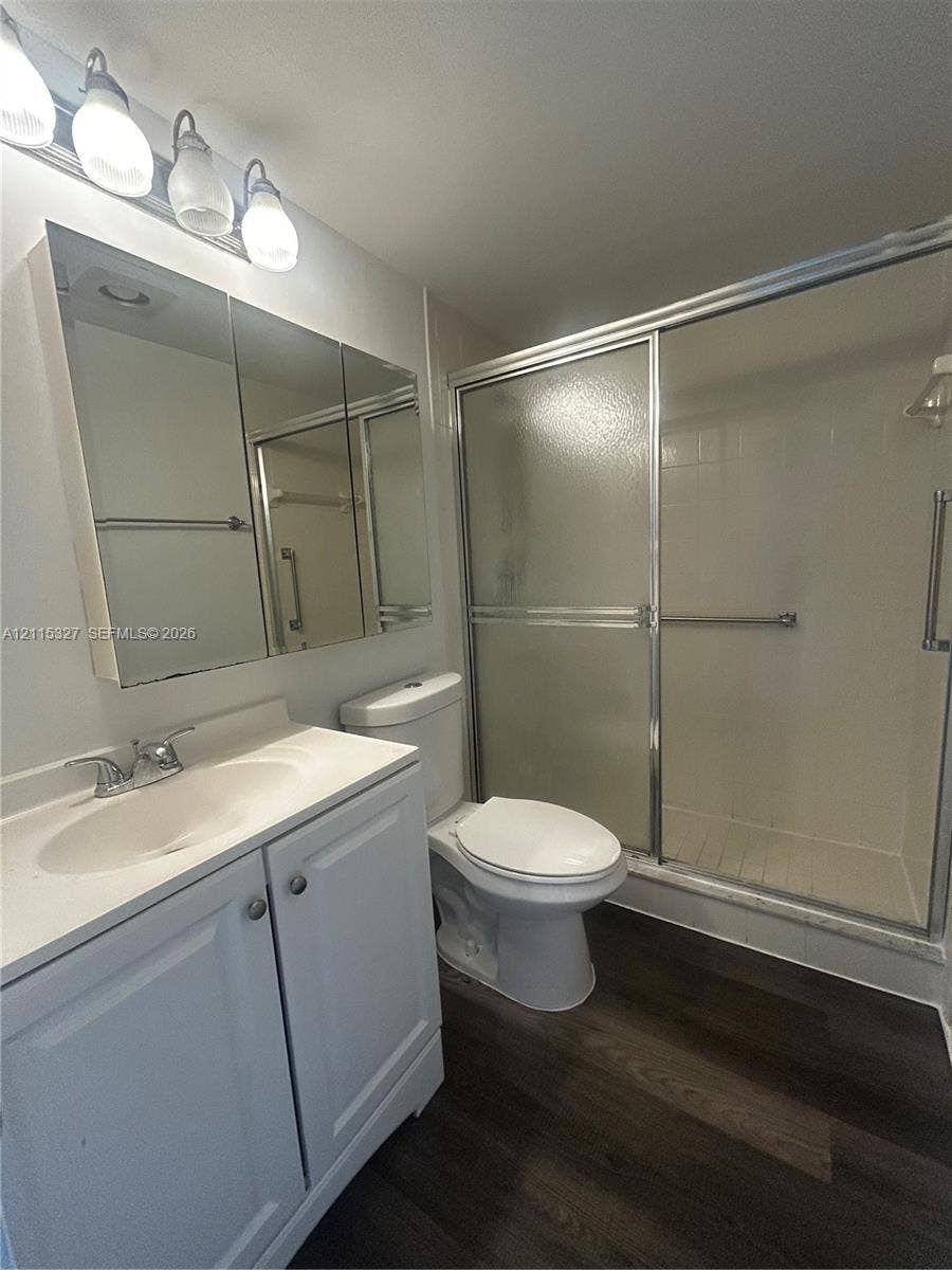 335 Brighton H, #H, Boca Raton, Boca Raton, FL 33434 Bathroom featuring a vanity with integrated sink, tri-fold mirrored medicine cabinet, four-light vanity fixture, enclosed walk-in shower, and dark wood-finish flooring