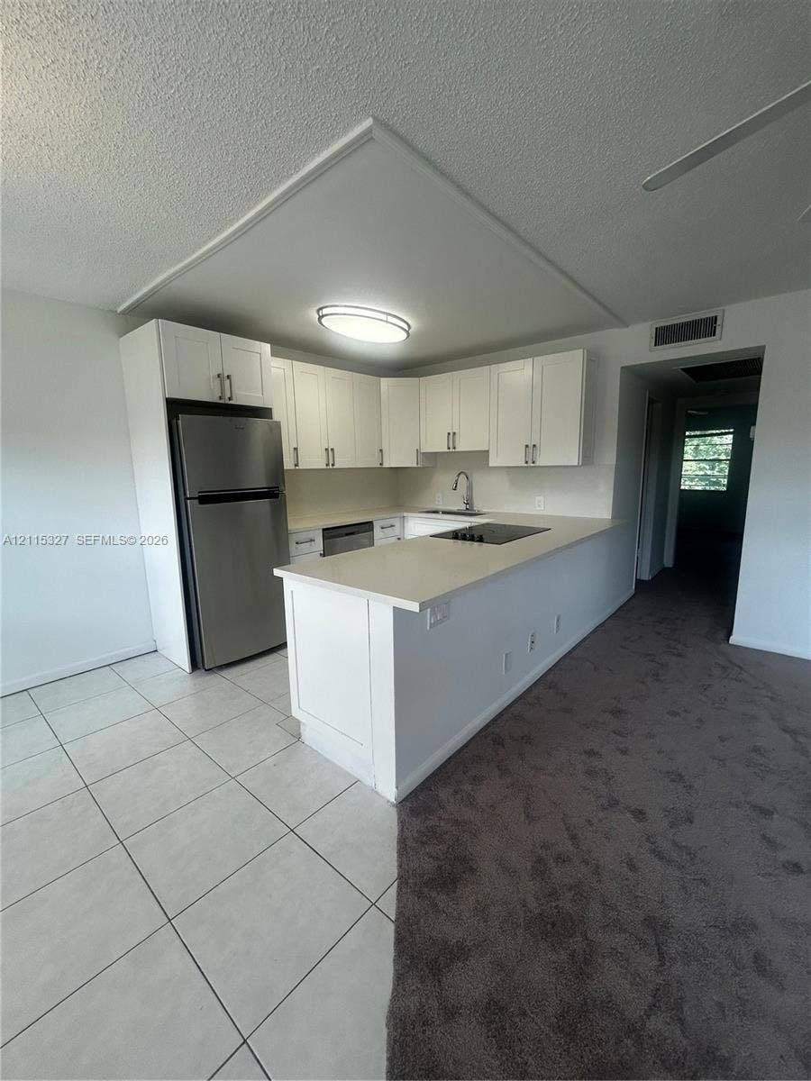 335 Brighton H, #H, Boca Raton, Boca Raton, FL 33434 Kitchen featuring white shaker-style cabinetry, a peninsula with stone-surface countertop, stainless steel refrigerator, and integrated cooktop