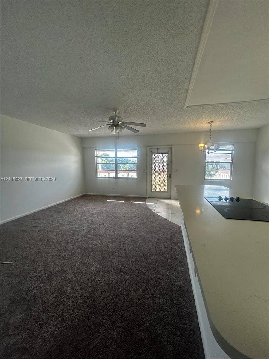 335 Brighton H, #H, Boca Raton, Boca Raton, FL 33434 Open-concept interior featuring wall-to-wall carpeting, a kitchen island with a cooktop, a ceiling fan, and multi-pane windows