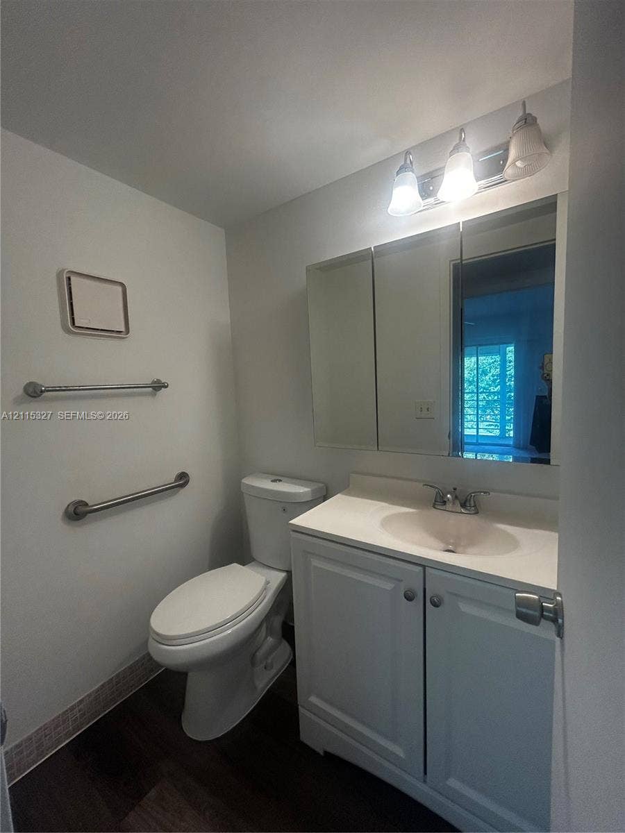 335 Brighton H, #H, Boca Raton, Boca Raton, FL 33434 Bathroom featuring a white vanity cabinet with an integrated sink, tri-panel mirrored medicine cabinet, three-light wall fixture, and wood-finish flooring