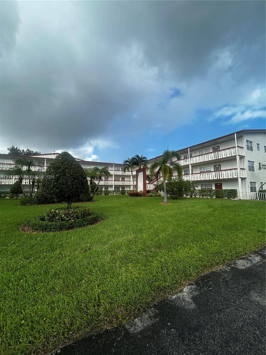 335 Brighton H, #H, Boca Raton, Boca Raton, FL 33434 Multi-story building featuring wrap-around railed balconies, expansive green lawn, and mature palm trees