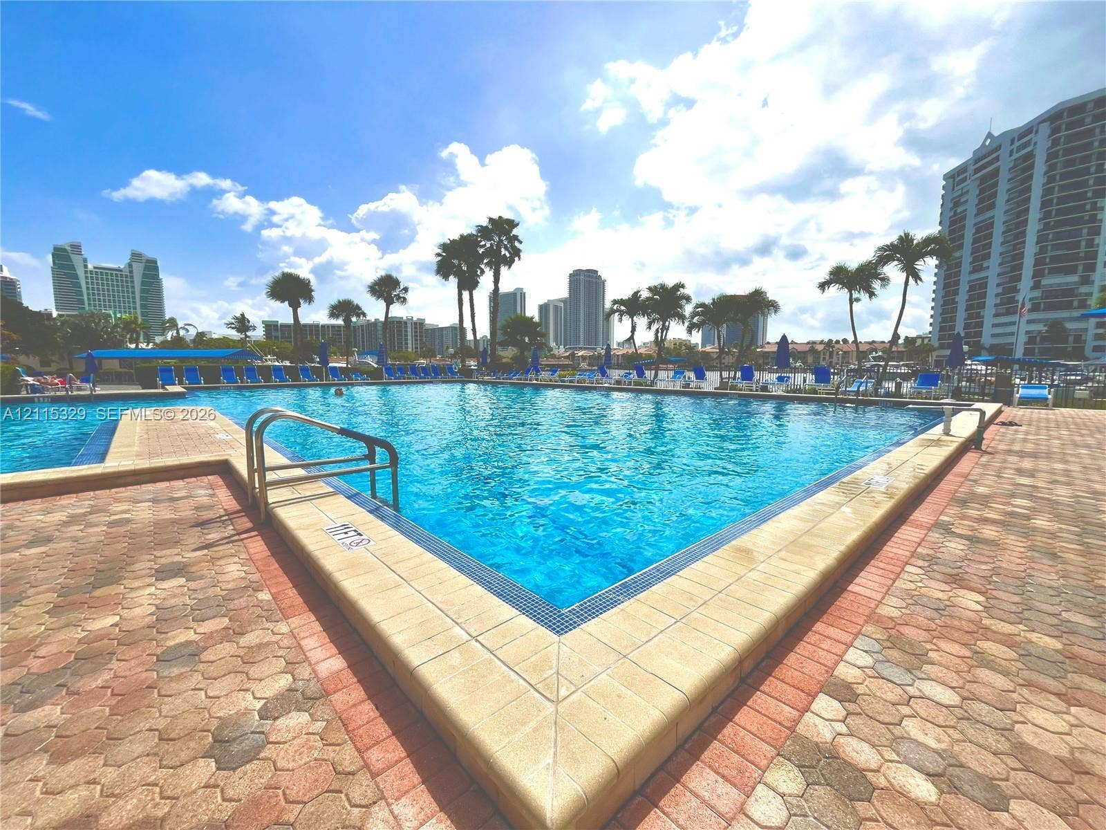 2500 Parkview Drive, #1705, Hallandale Beach, Hallandale Beach, FL 33009 Swimming pool with tiled coping and metal railings, surrounded by a geometric paver deck and mature palm trees