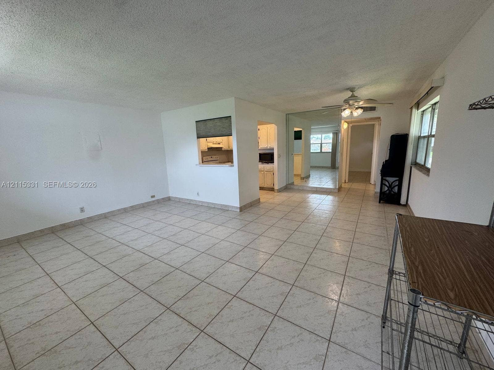 22 Valencia A, Delray Beach, FL 33446 Open-concept interior featuring light-colored ceramic tile flooring, a pass-through window to the kitchen, mirrored wall accents, and a ceiling fan with integrated lighting