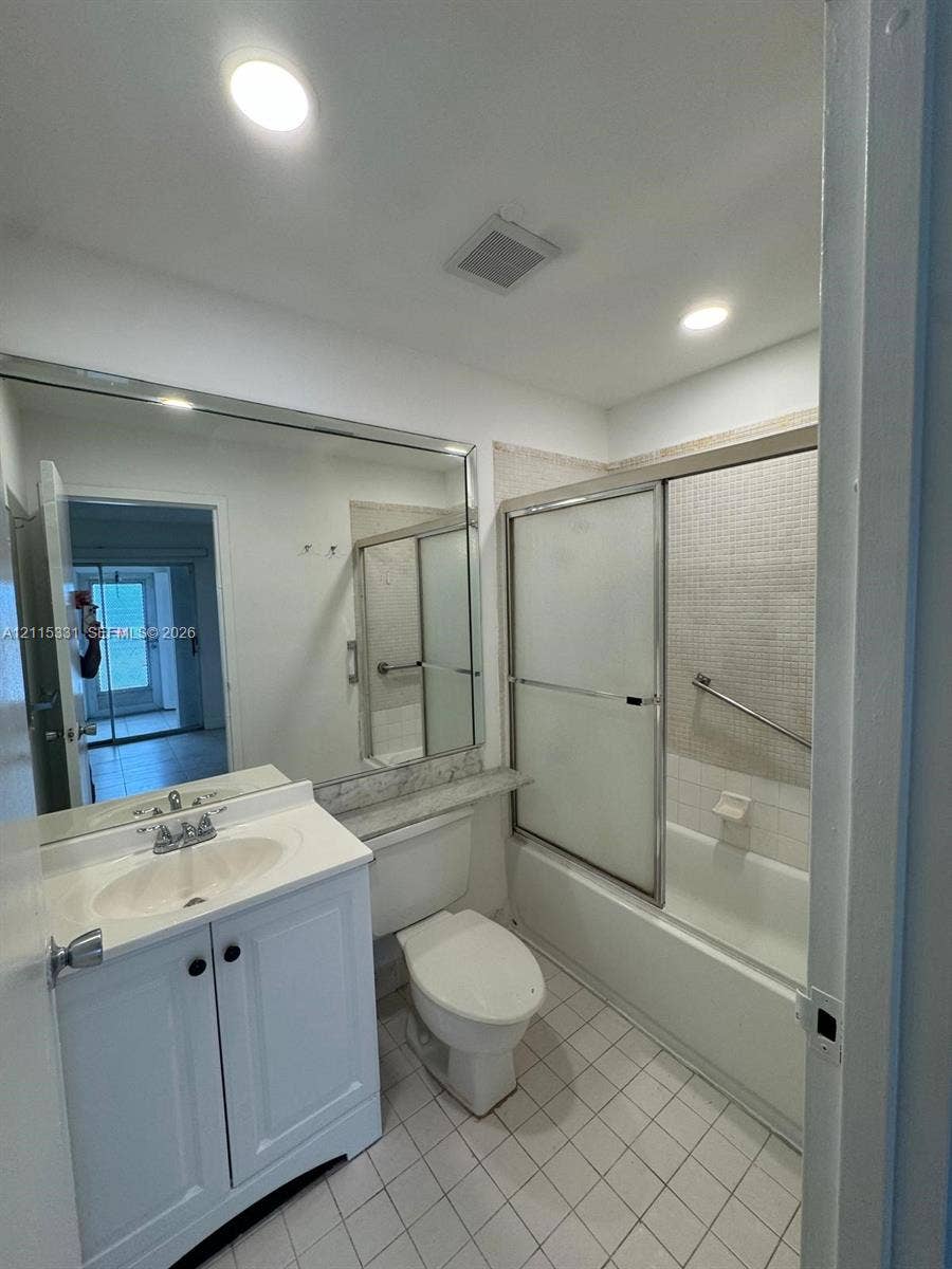 22 Valencia A, Delray Beach, FL 33446 Bathroom featuring a vanity with an integrated sink and stone-finish countertop, full-width wall mirror, tub-shower combination with sliding glass doors, mosaic-tile shower surround, and square-tile flooring