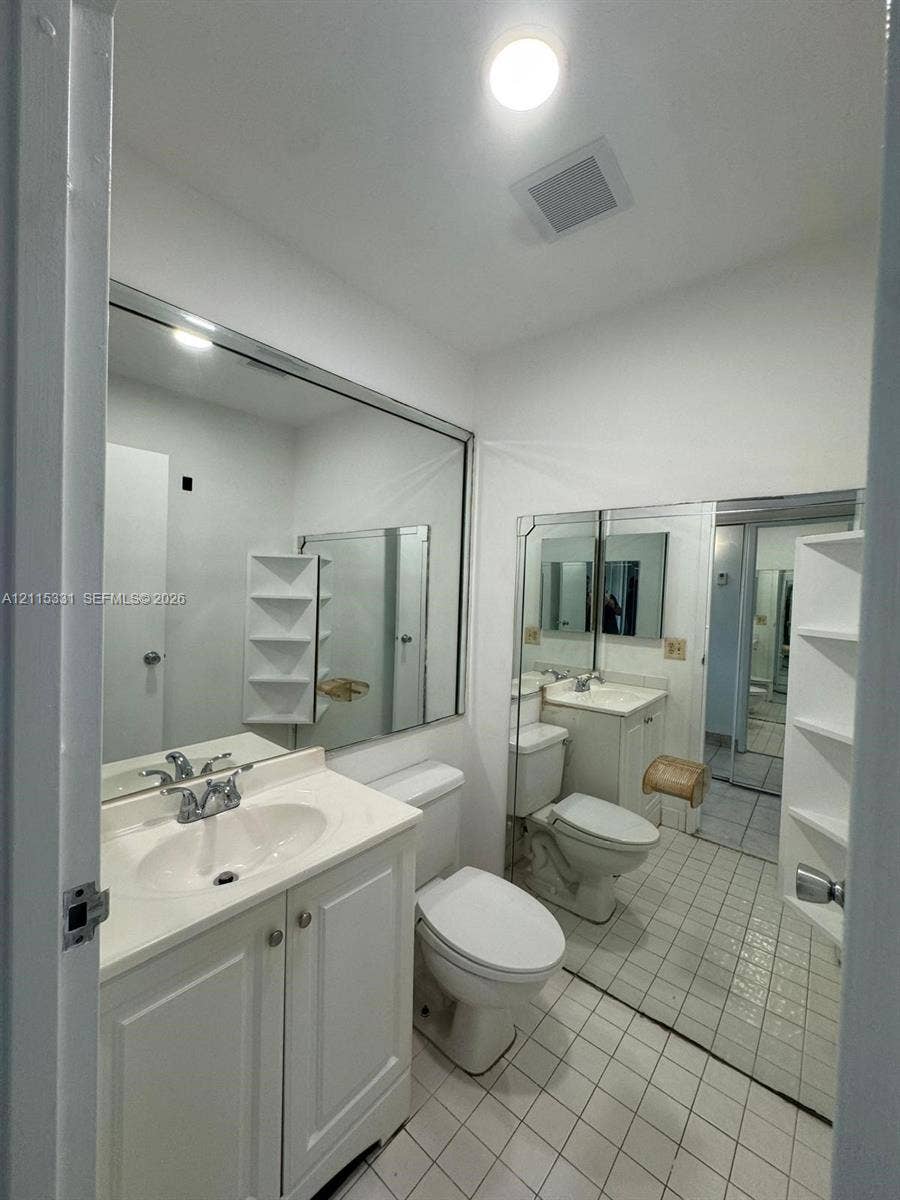 22 Valencia A, Delray Beach, FL 33446 Bathroom featuring a white vanity cabinet with a integrated sink, large wall-mounted mirrors, tile flooring, and built-in shelving