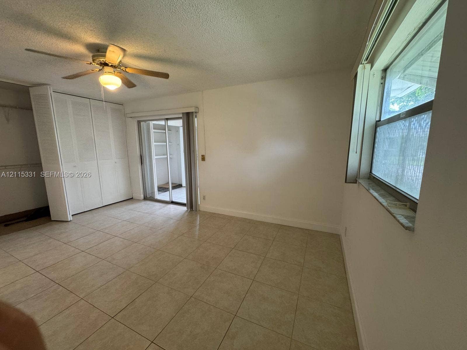22 Valencia A, Delray Beach, FL 33446 Interior space featuring neutral floor tiling, louvered-door closets, a ceiling fan with integrated lighting, and a sliding glass door providing access to an exterior enclosure
