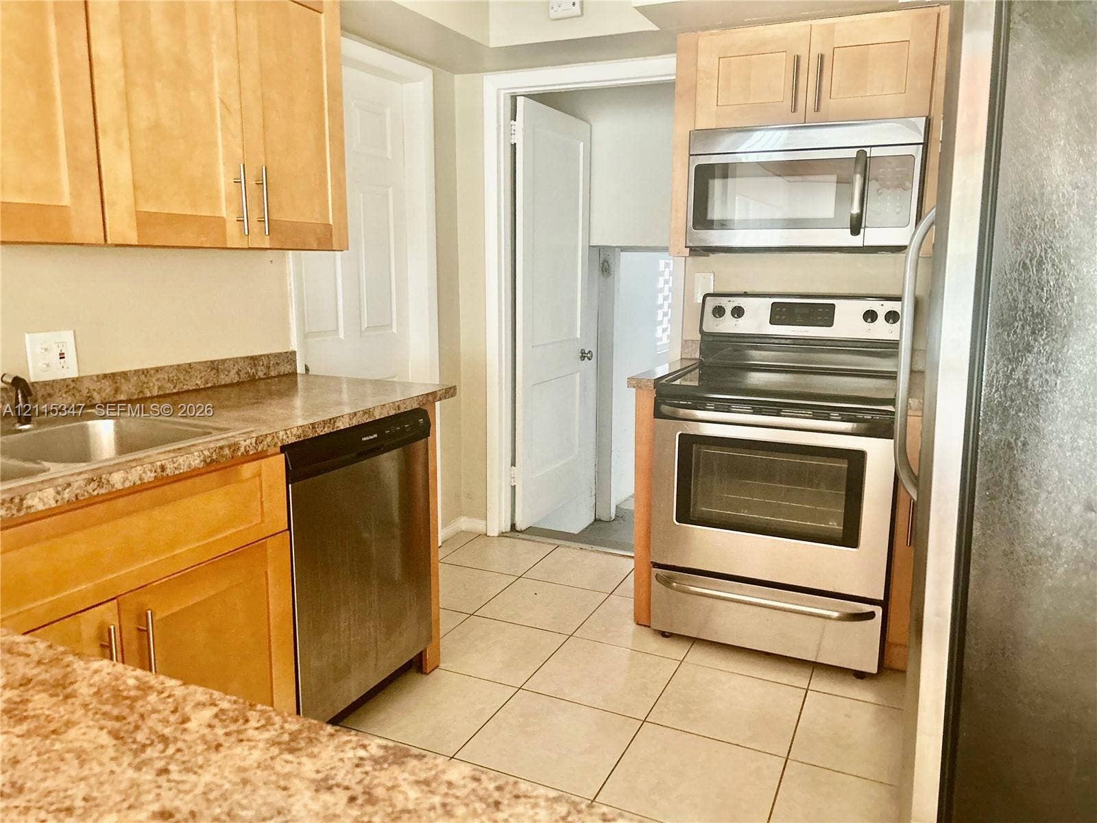 Kitchen featuring light wood cabinetry, stone-finish laminate countertops, tile flooring, and stainless steel appliances including a range, microwave, and dishwasher