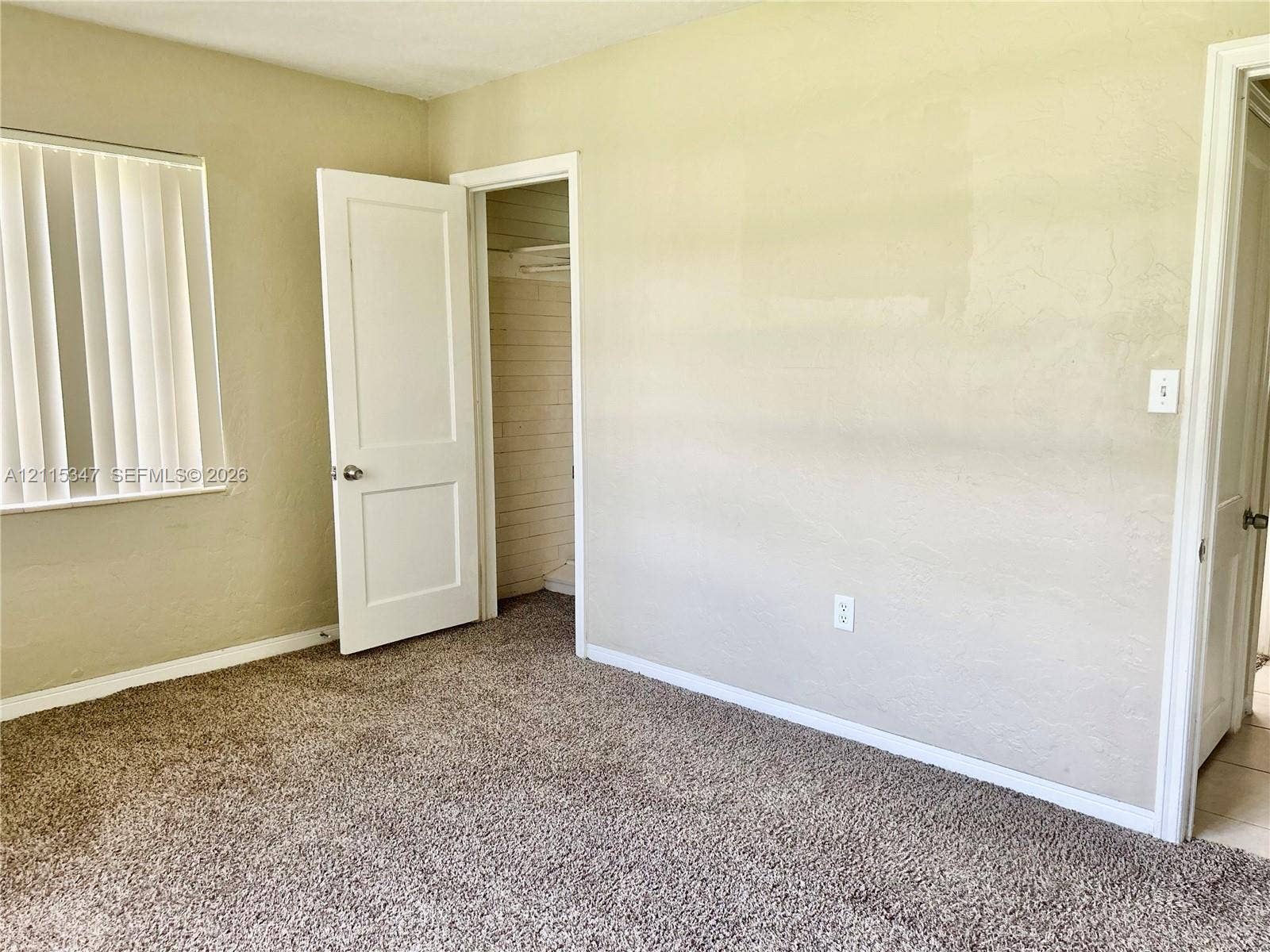 Neutral wall tones, wall-to-wall carpeting, vertical window blinds, and interior doors featuring brushed metal hardware
