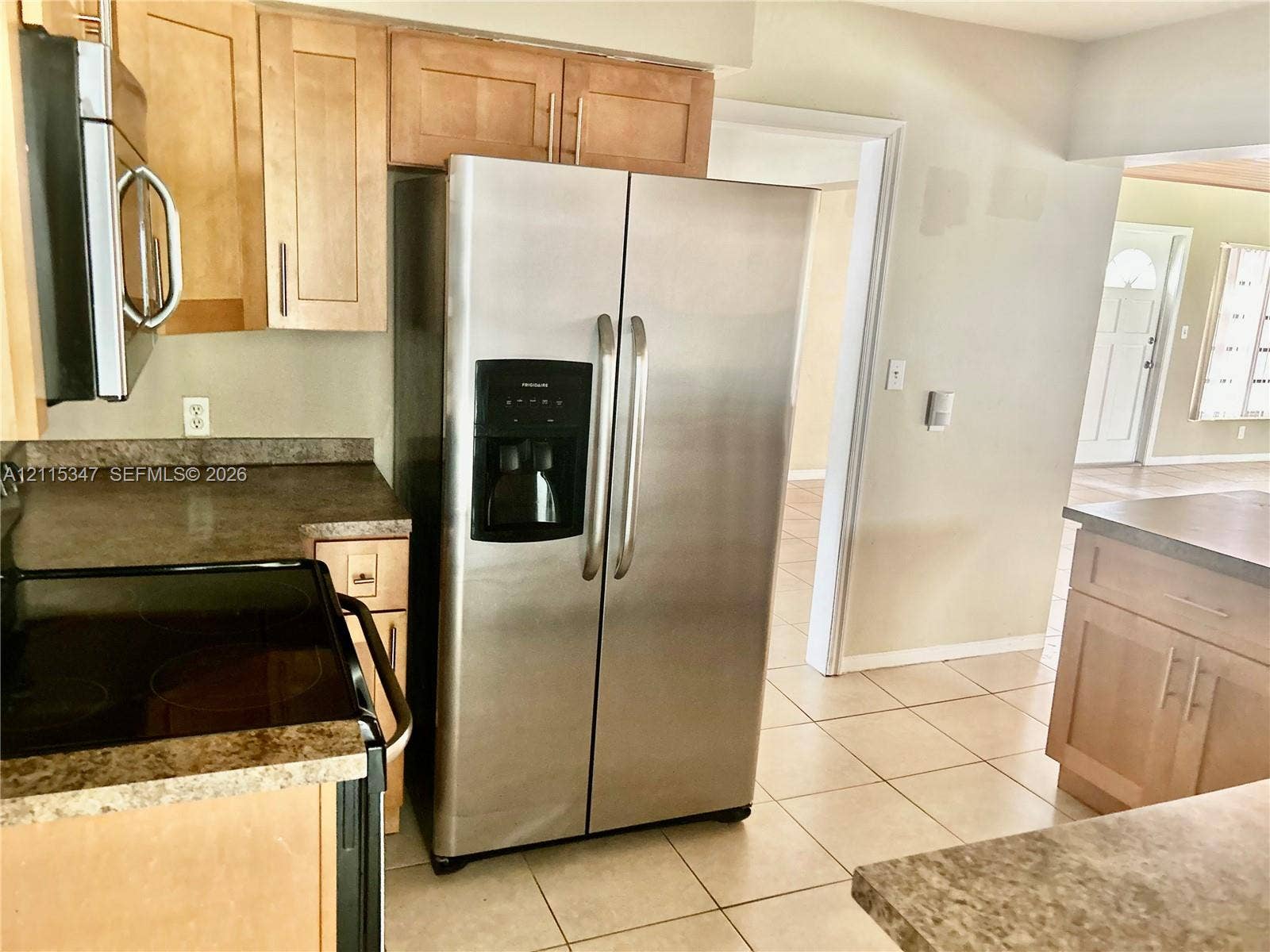 Kitchen featuring light-finish cabinetry, neutral solid-surface countertops, stainless steel side-by-side refrigerator, and tile flooring