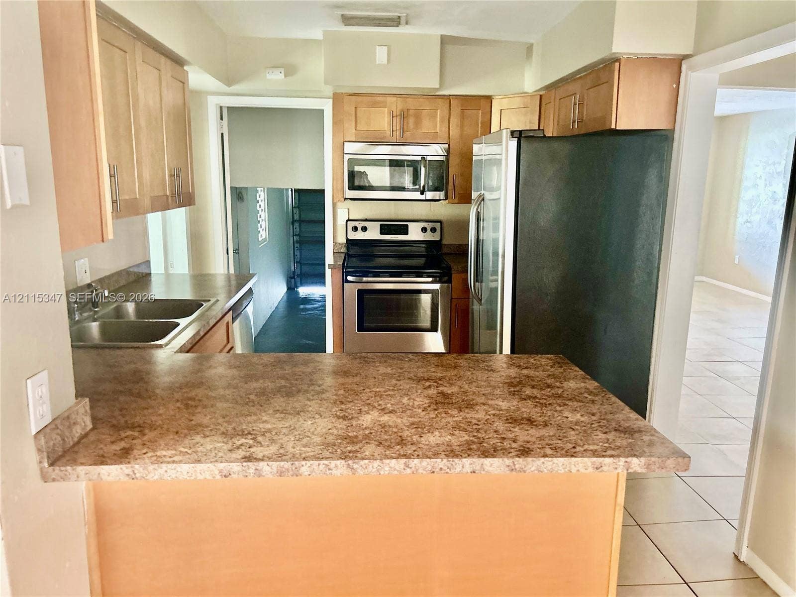 Kitchen featuring light wood cabinetry, stone-pattern laminate countertops, stainless steel appliances, and a double-basin sink