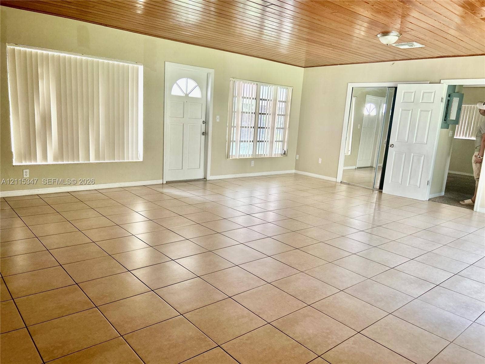 Expansive room featuring wood-plank ceiling, neutral ceramic tile flooring, multi-pane windows, and a classic-style entry door