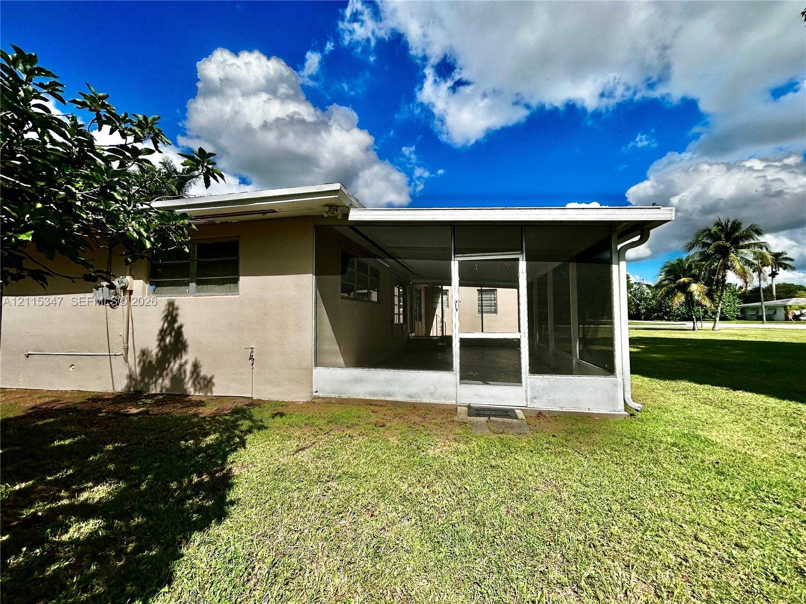 Stucco exterior featuring a screened-in lanai with aluminum framing and an expansive rear lawn