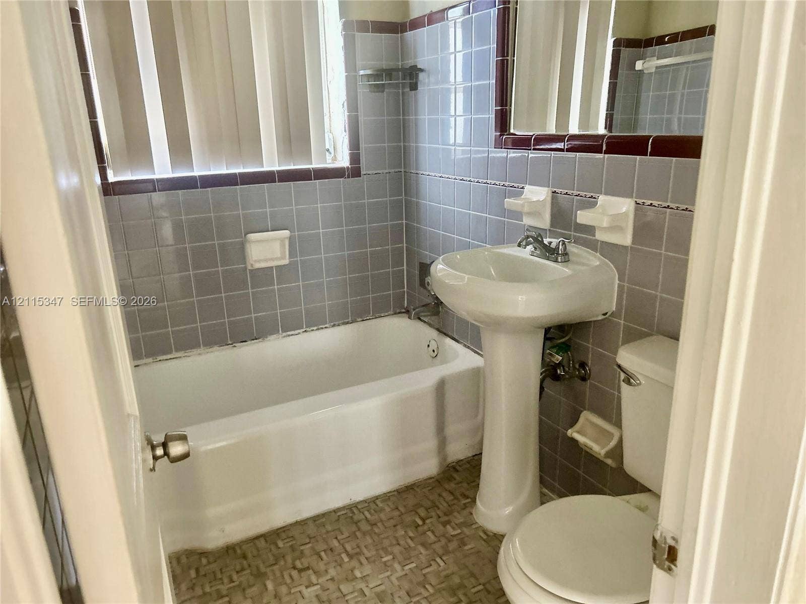 Bathroom featuring a white pedestal sink, a standard tub with shower head, patterned tile flooring, and light-toned wall tile with dark decorative trim