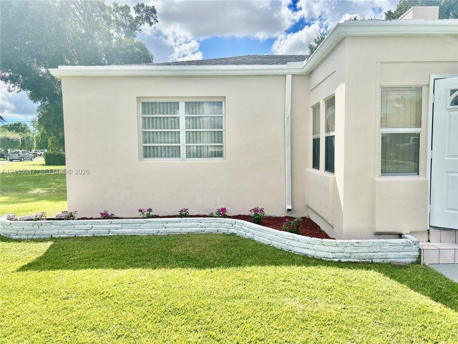 Stucco exterior featuring multi-pane windows and a curved, painted brick garden border