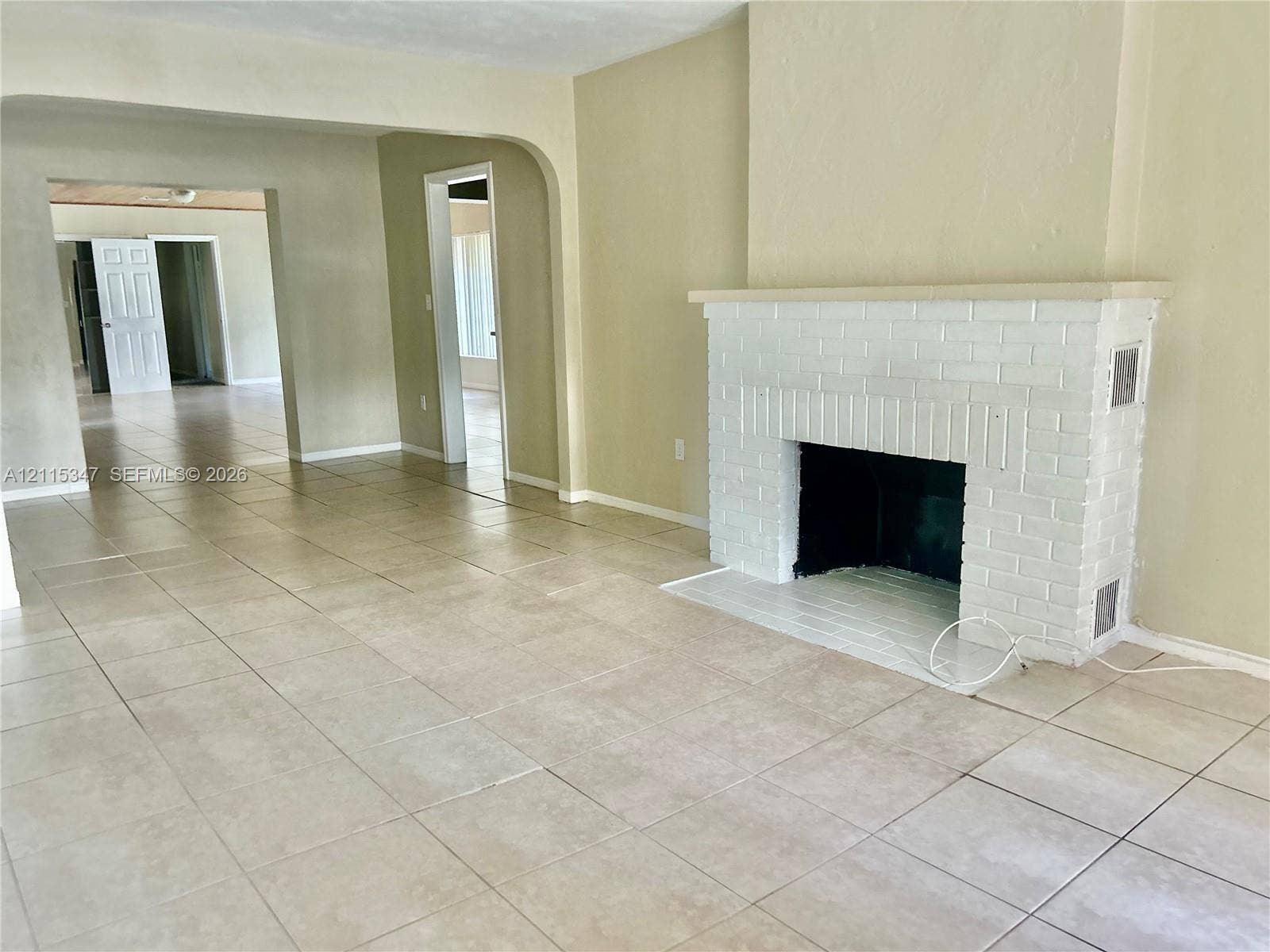 White painted brick fireplace, tile flooring, arched doorways, and neutral wall tones