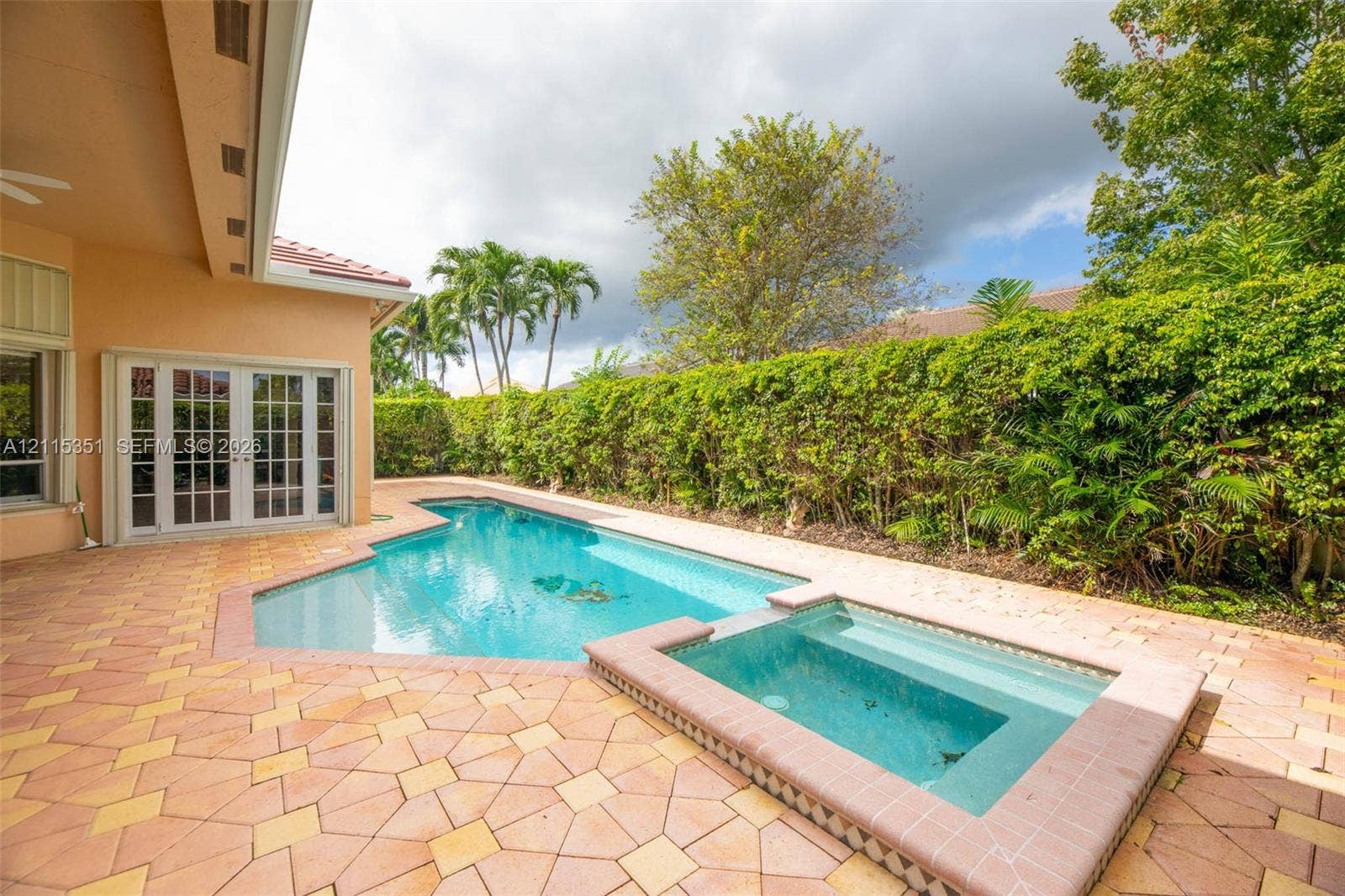 13845 NW 20th Street, Pembroke Pines, FL 33028 In-ground swimming pool and attached spa with a paved stone deck, covered patio, and perimeter privacy hedging