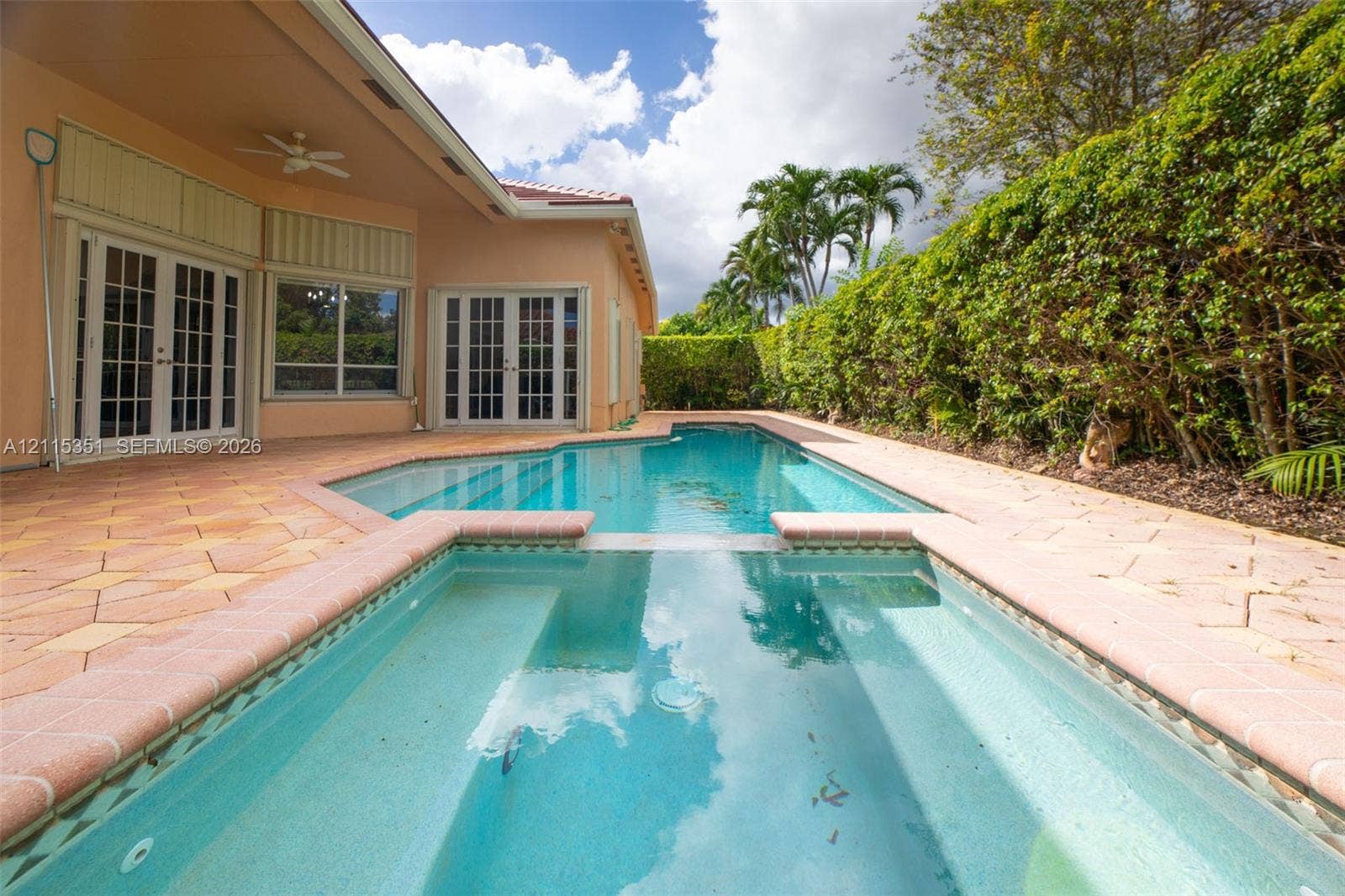 13845 NW 20th Street, Pembroke Pines, FL 33028 In-ground swimming pool with integrated spa, paver patio, covered porch with ceiling fan, and surrounding privacy hedging
