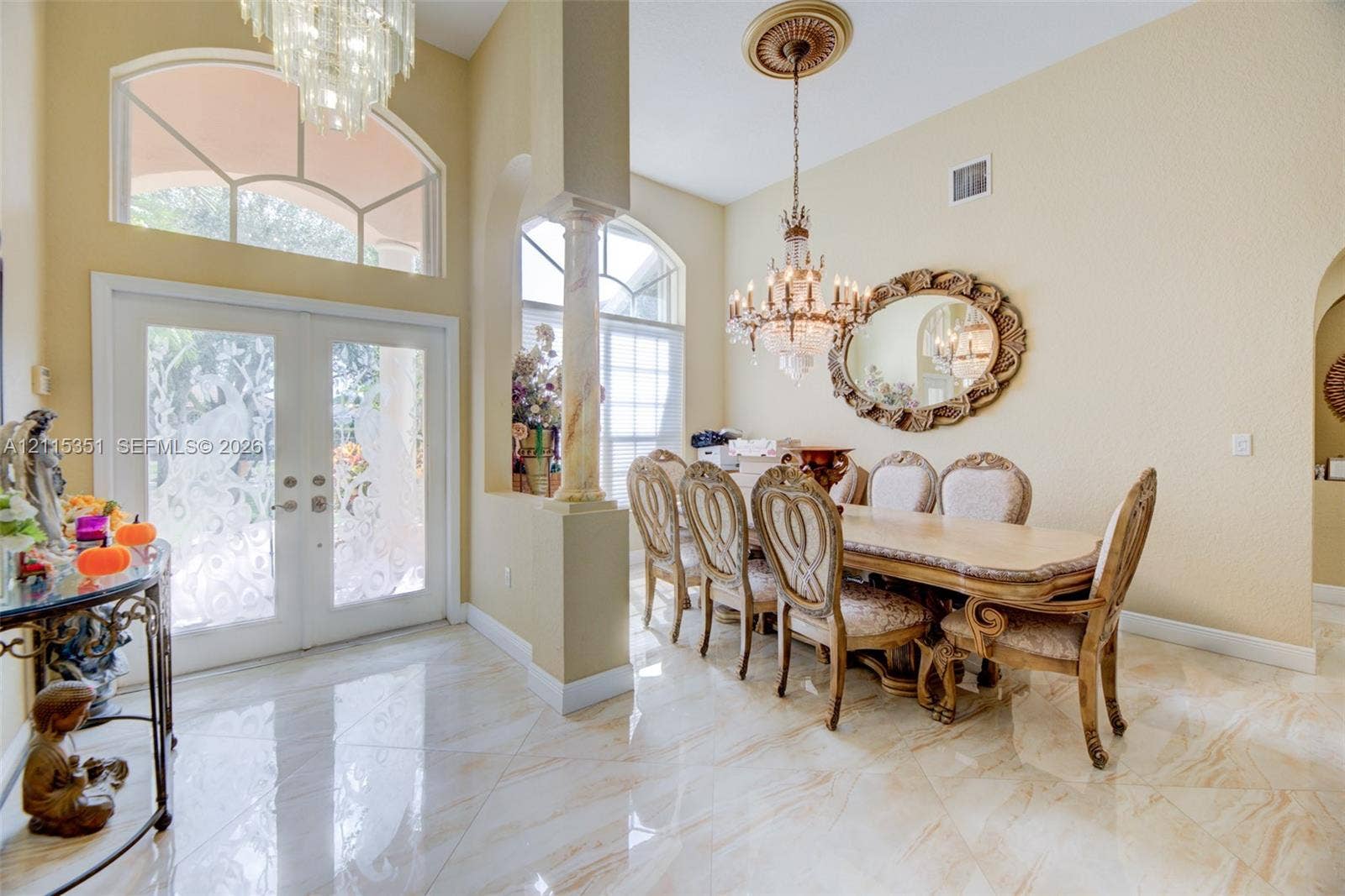 13845 NW 20th Street, Pembroke Pines, FL 33028 Foyer and dining space featuring large-format tile flooring, dual glass-paneled entry doors with arched transom windows, a decorative column, and dual crystal chandeliers