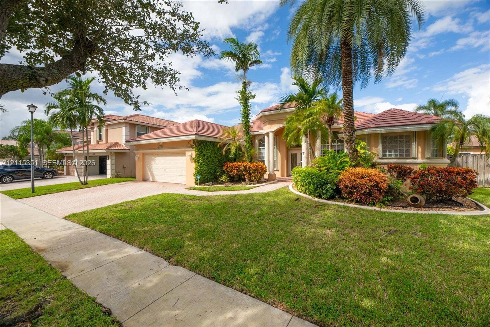 13845 NW 20th Street, Pembroke Pines, FL 33028 Stucco exterior residence featuring a multi-hip tile roof, paved driveway, column-accented entryway, and mature tropical landscaping