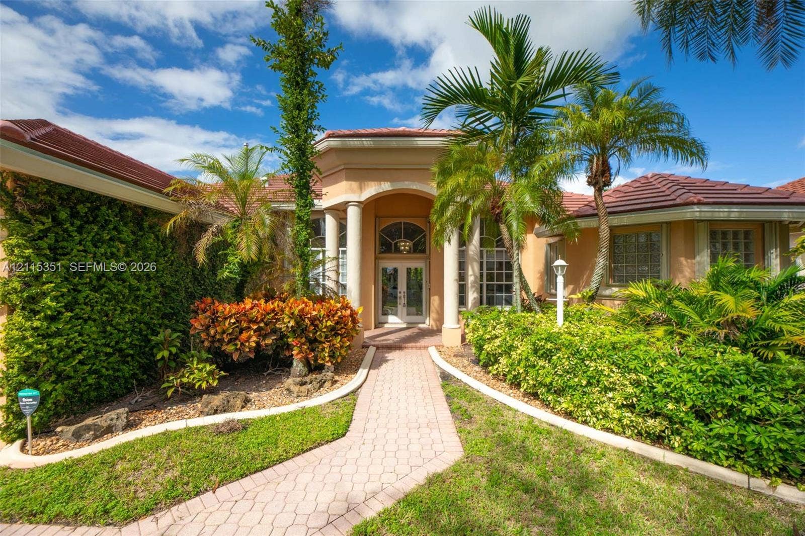 13845 NW 20th Street, Pembroke Pines, FL 33028 Stucco exterior featuring a tiled hip roof, arched entryway with dual columns, and a paver walkway leading to glass-paneled double doors