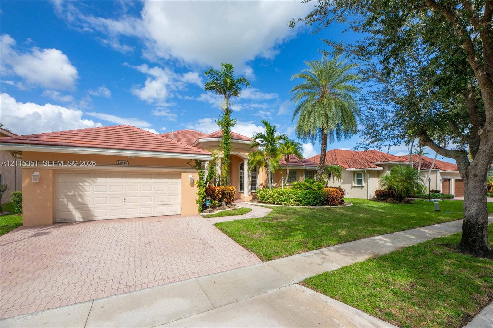 13845 NW 20th Street, Pembroke Pines, FL 33028 Stucco exterior featuring a red tile roof, attached two-car garage, brick paver driveway, and mature landscaping