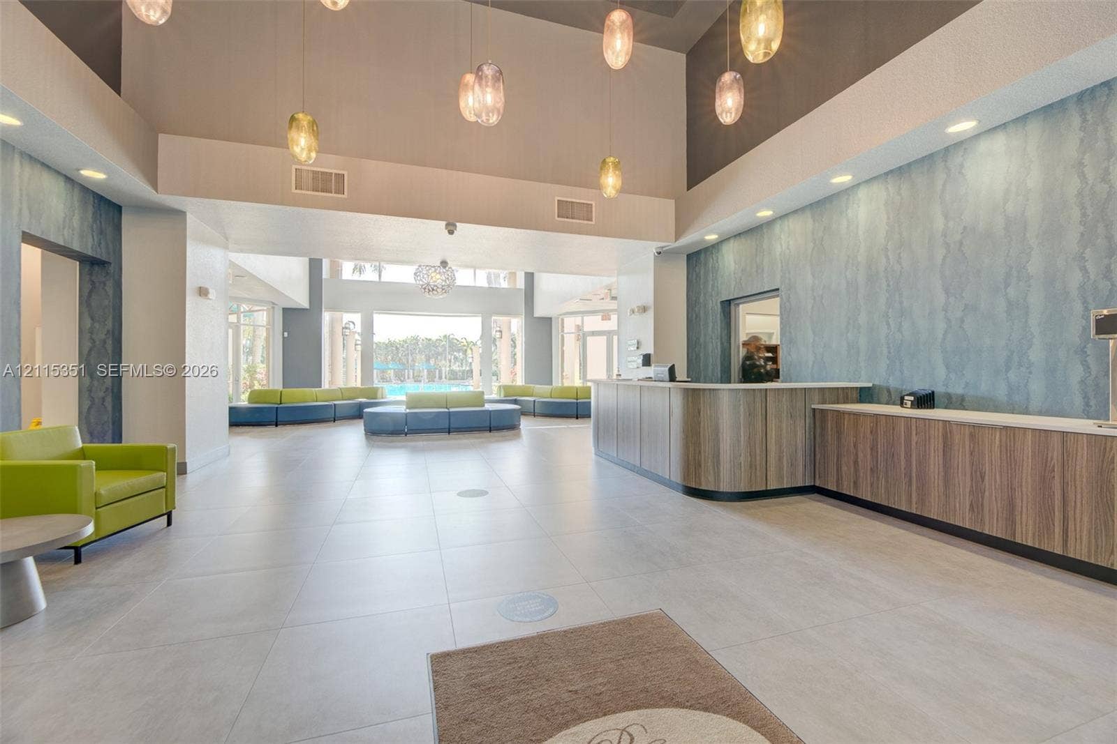 13845 NW 20th Street, Pembroke Pines, FL 33028 Grand lobby featuring high ceilings, large-format tile flooring, textured accent wall, integrated custom reception desk, and multi-tier pendant lighting