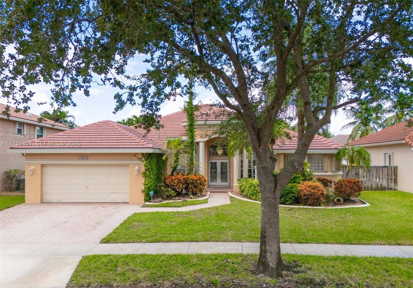13845 NW 20th Street, Pembroke Pines, FL 33028 Single-story residence featuring a tiled roof, arched entryway with decorative columns, brick-paver driveway, and manicured landscaping