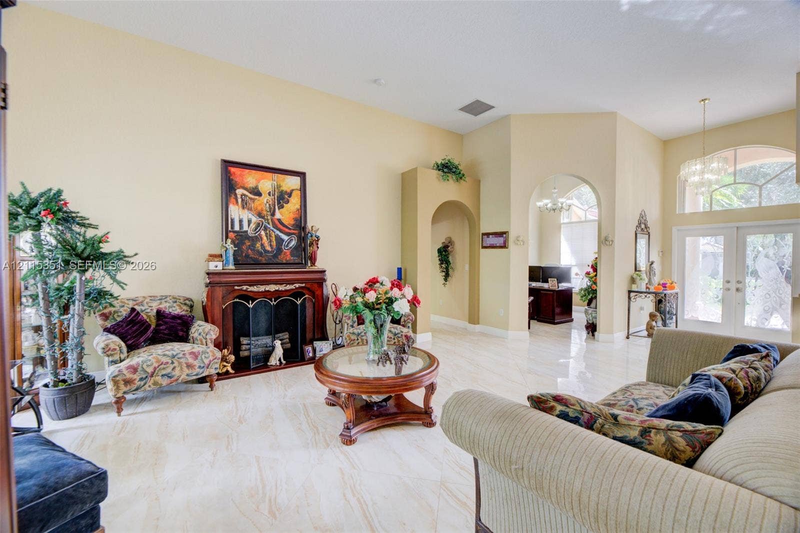 13845 NW 20th Street, Pembroke Pines, FL 33028 Living space featuring vaulted ceilings, polished tile flooring, a fireplace with a decorative mantel, arched entryways, and glass-paned double entry doors with an arched transom window