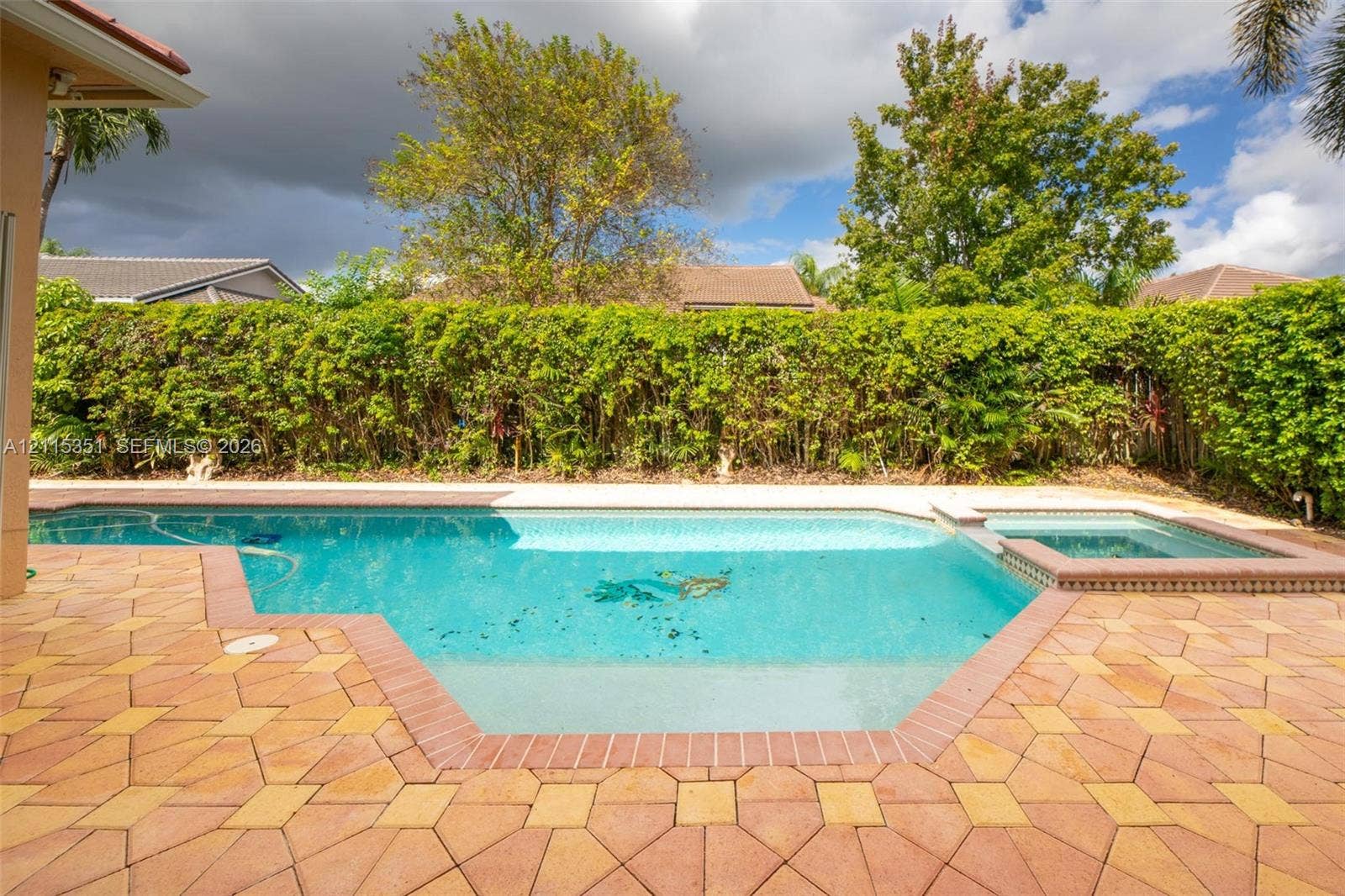 13845 NW 20th Street, Pembroke Pines, FL 33028 Outdoor pool with integrated spa, bordered by patterned paver decking and high-density privacy shrubbery