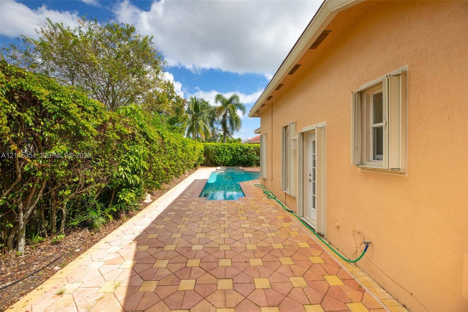 13845 NW 20th Street, Pembroke Pines, FL 33028 Outdoor living area featuring patterned paver hardscaping, a geometric swimming pool, exterior wall shutters, and manicured hedge landscaping