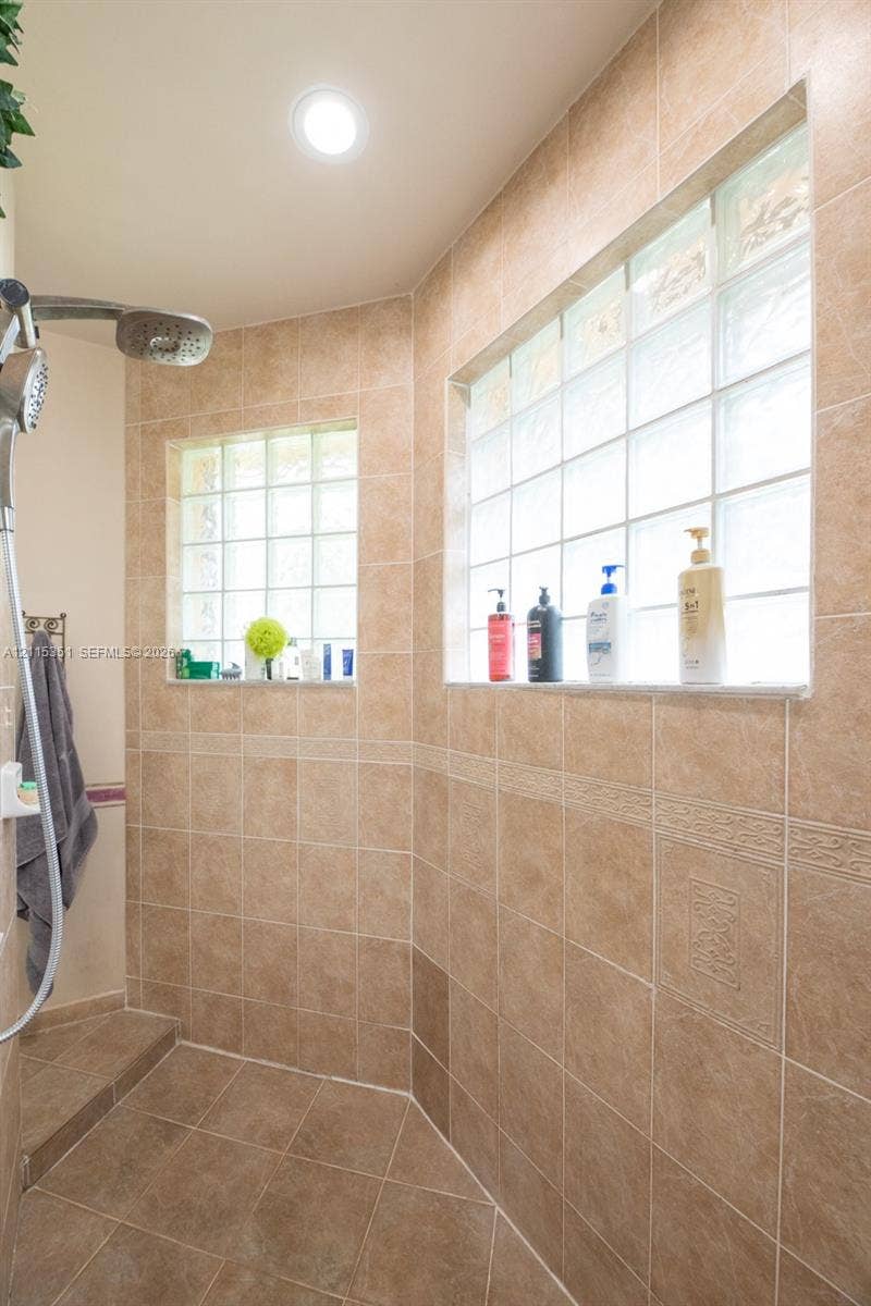 13845 NW 20th Street, Pembroke Pines, FL 33028 Walk-in shower featuring floor-to-ceiling tile, decorative accent trim, glass block windows, and a stainless steel shower head