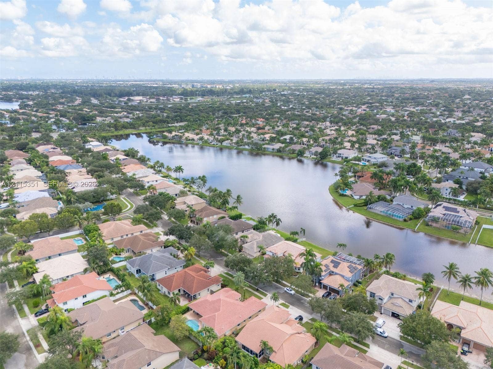 13845 NW 20th Street, Pembroke Pines, FL 33028 Aerial perspective of a lakeside community featuring mature palm trees and residential properties with multi-pitch tiled roofing