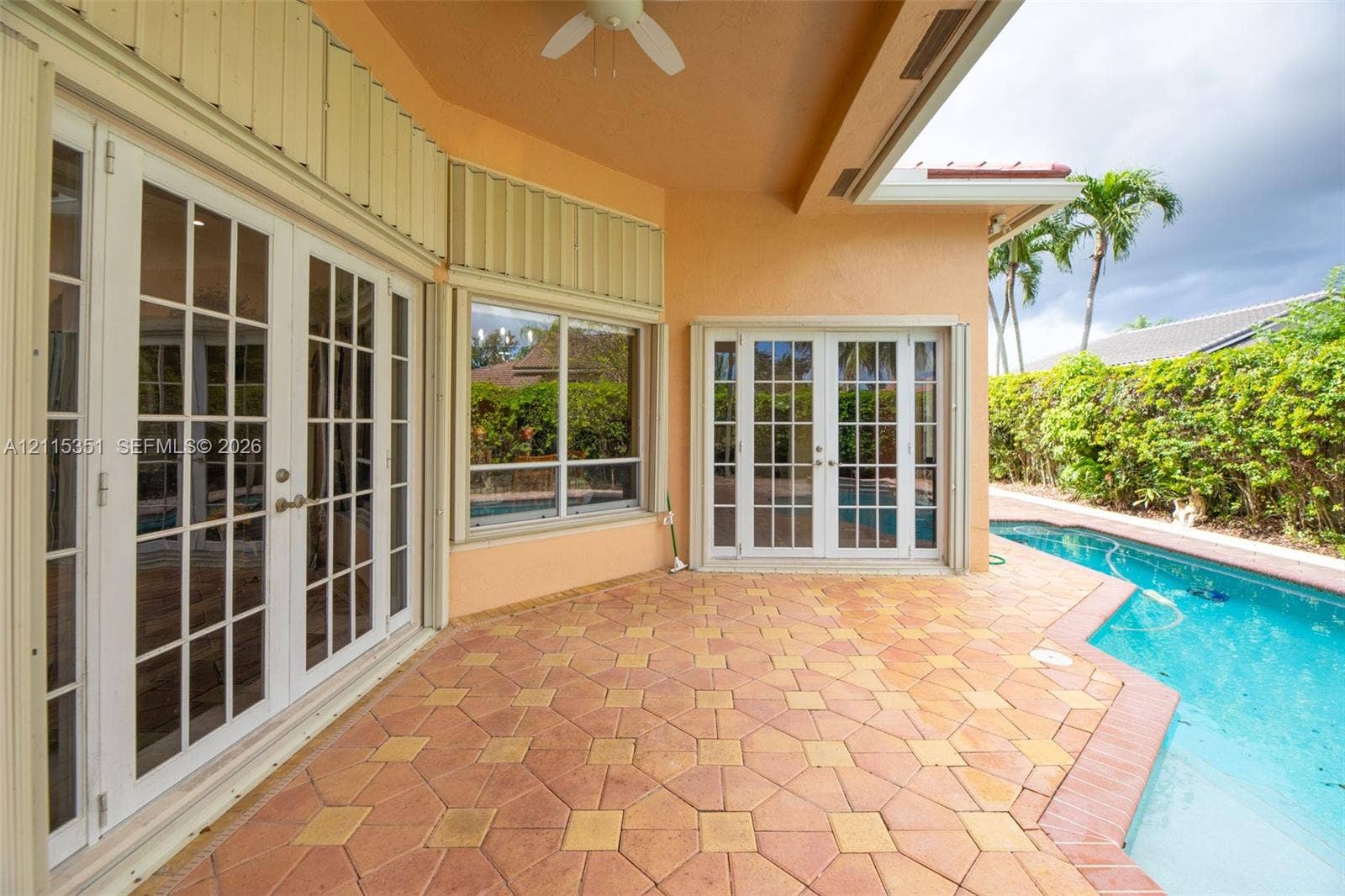 13845 NW 20th Street, Pembroke Pines, FL 33028 Covered patio featuring patterned stone pavers, multiple sets of white French doors, integrated ceiling fan, and an in-ground swimming pool
