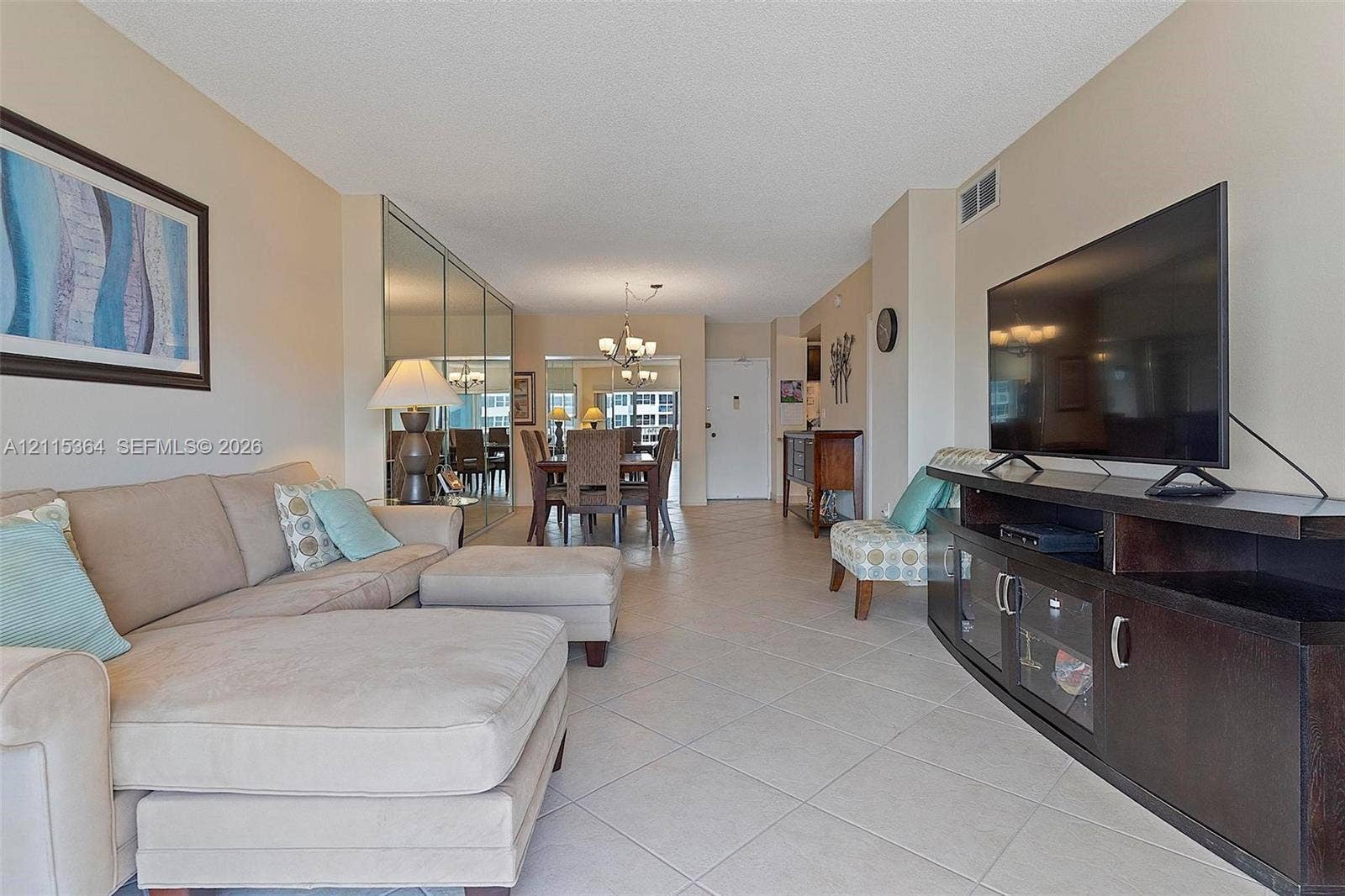 1980 S Ocean Drive, #20A, Hallandale Beach, Hallandale Beach, FL 33009 Open-concept living area featuring large-format tile flooring, floor-to-ceiling mirrored wall panels, and a multi-arm chandelier fixture