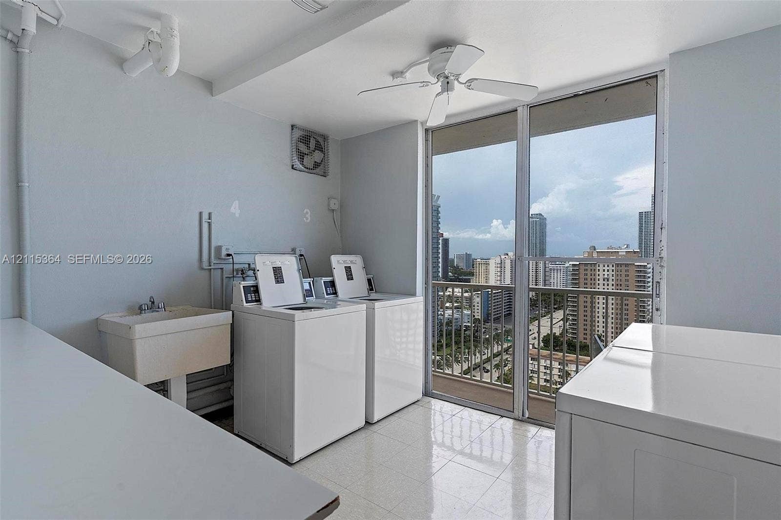 1980 S Ocean Drive, #20A, Hallandale Beach, Hallandale Beach, FL 33009 Laundry area featuring tile flooring, a wall-mounted utility sink, ceiling-mounted fan, and floor-to-ceiling glass sliding doors opening to an exterior balcony