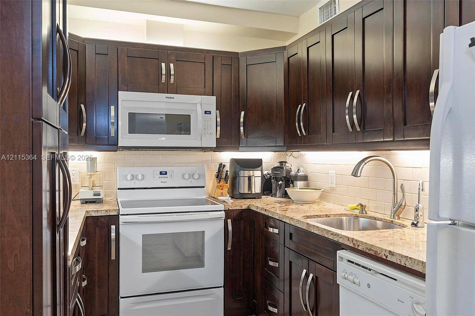 1980 S Ocean Drive, #20A, Hallandale Beach, Hallandale Beach, FL 33009 Kitchen featuring dark wood-finish cabinetry, stone countertops, a light-toned subway tile backsplash, and under-cabinet task lighting