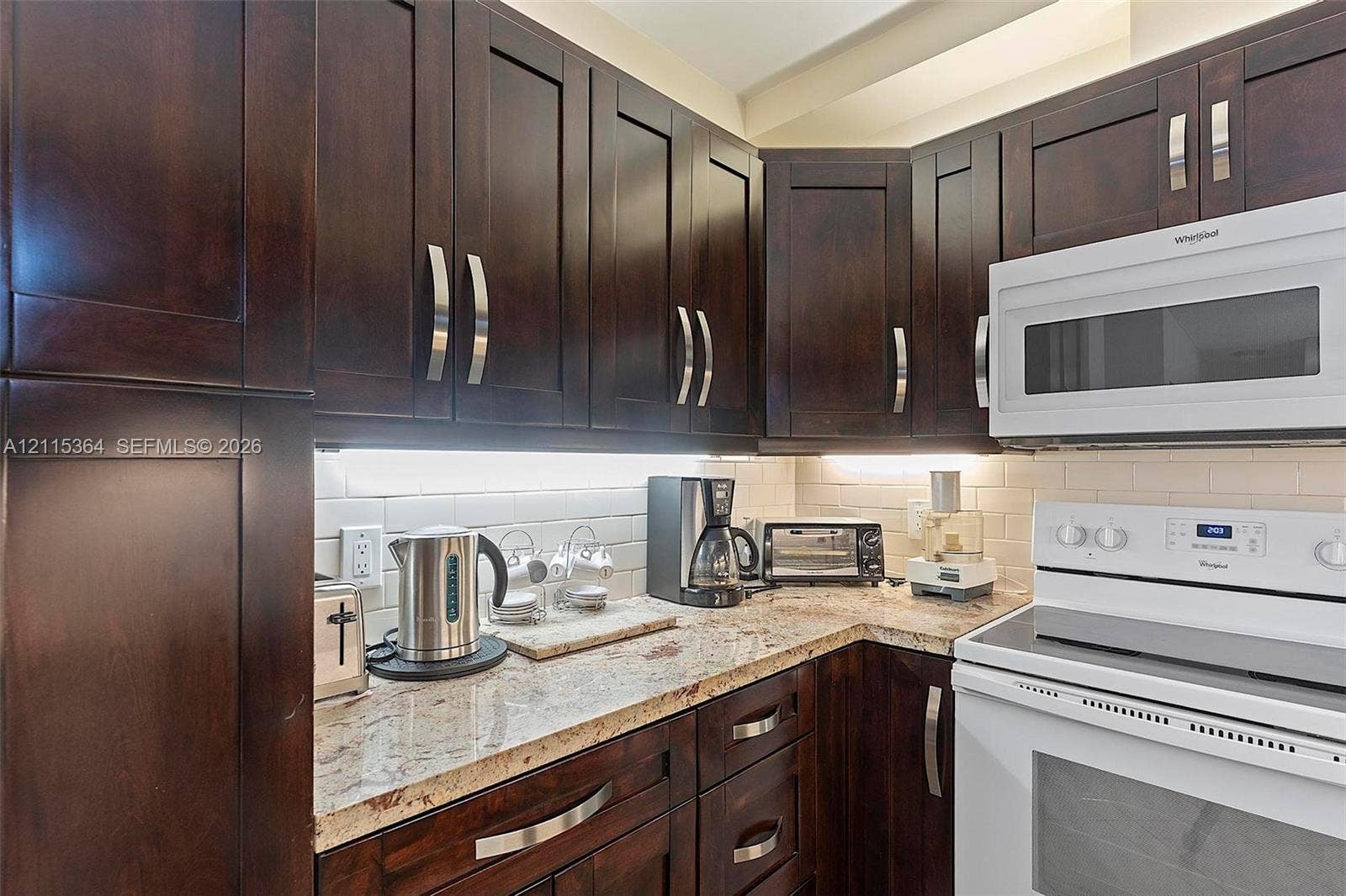 1980 S Ocean Drive, #20A, Hallandale Beach, Hallandale Beach, FL 33009 Dark-stained wood cabinetry, stone countertops, integrated under-cabinet lighting, subway tile backsplash, and white appliance suite